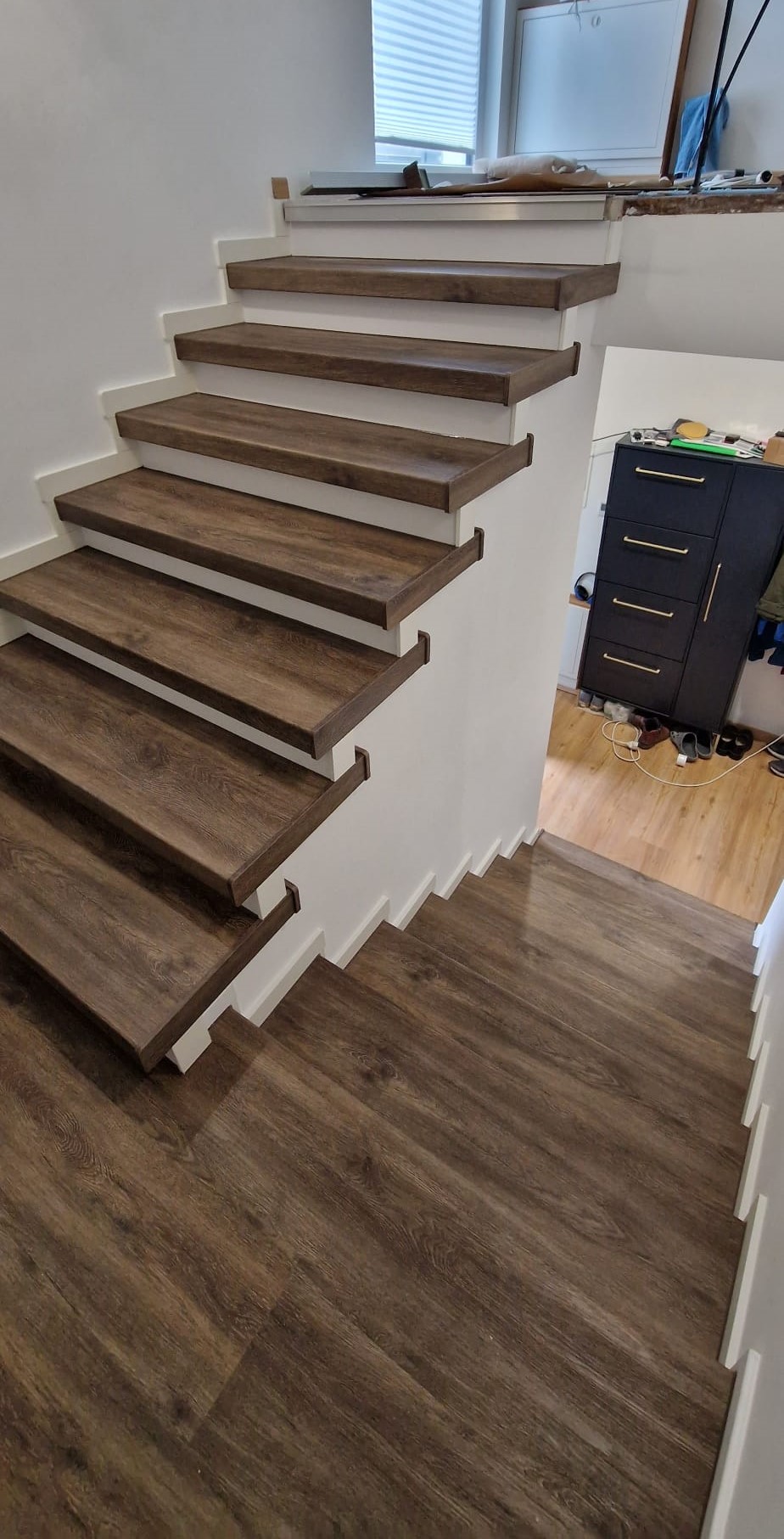 Treppenrenovierung in Erlangen, vollendetes Projekt: Vinyl-Belag in dunkler Eiche-Optik, dunkle Verkleidung für die Stufenkanten und weiße Sockelleisten an der Wand.
