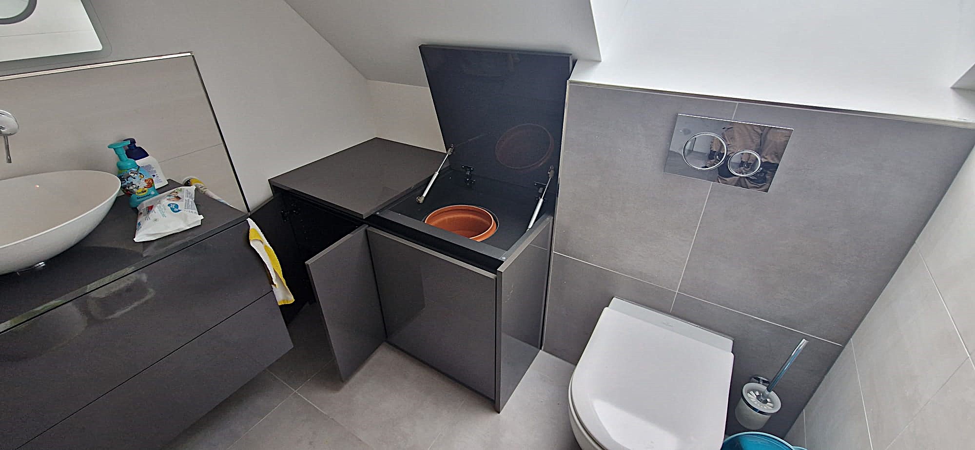 Grauer Badezimmer-Einbauschrank unter Dachschräge: Links normaler Schrank mit Doppeltür, rechts Klappe als Zugang zum Wäscheschacht.