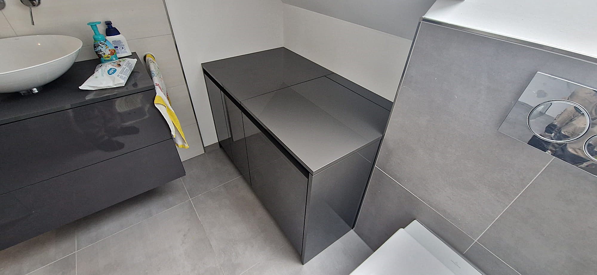 Badezimmerschrank nach Maß in Form einer Kommode aus dunkelgrauem Hochglanz-HPL unter einer Dachschräge.