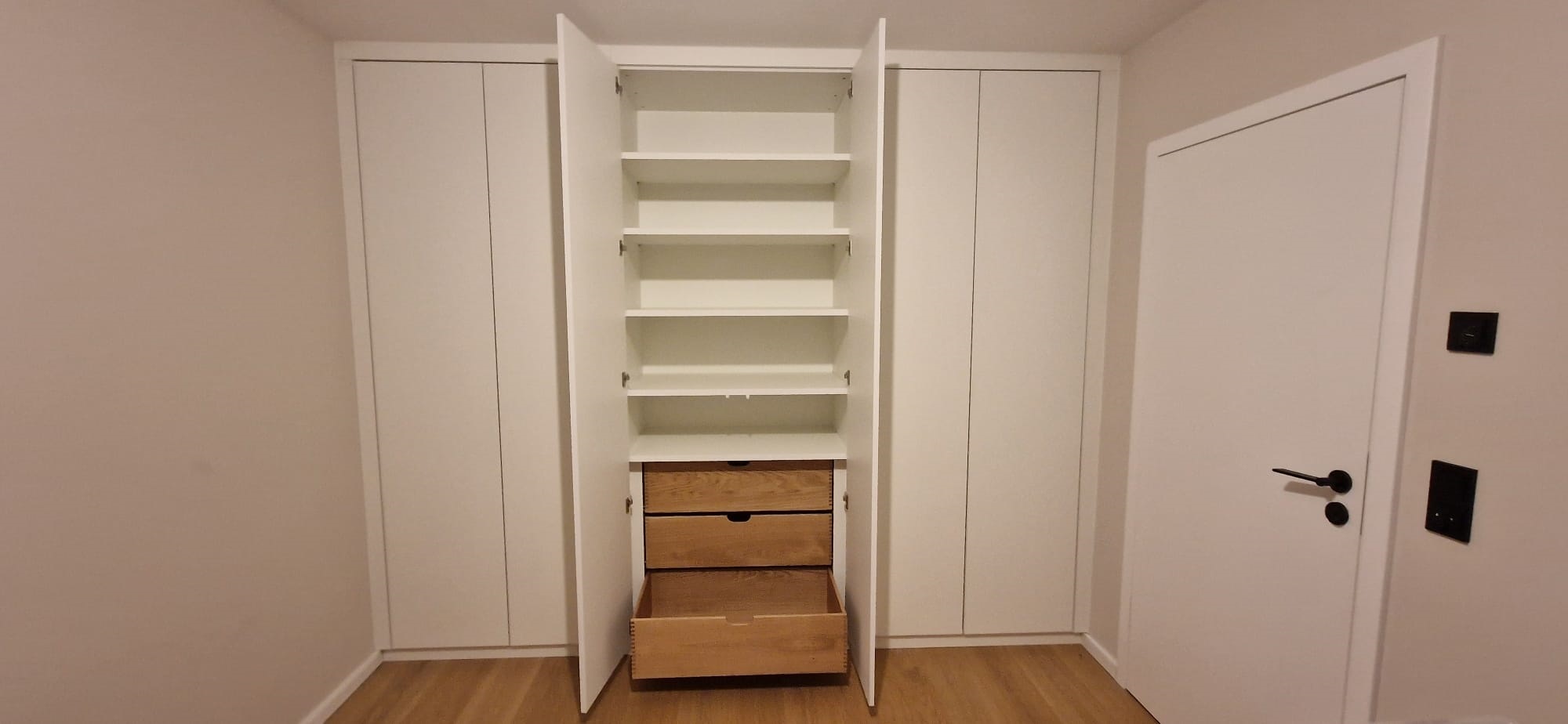 Weißer Einbauschrank Kinderzimmer: Die geöffneten mittleren Türen geben den Blick auf einen weißen Korpus mit Einlegeböden sowie 3 Schubladen aus Massivholz frei, die normalerweise hinter den Türen versteckt sind.