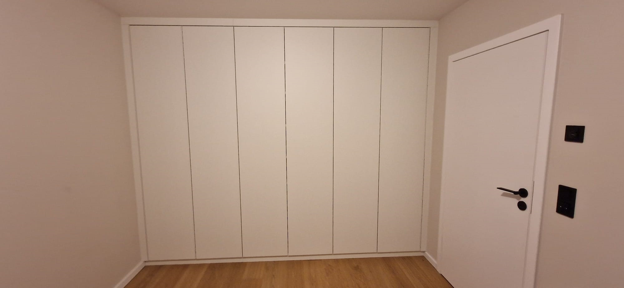 Weißer Einbauschrank Kinderzimmer mit geschlossenen Türen. Der Schrank nach Maß nutzt die Wand bis auf den letzten Zentimeter aus und wirkt selbst wie eine Wand.