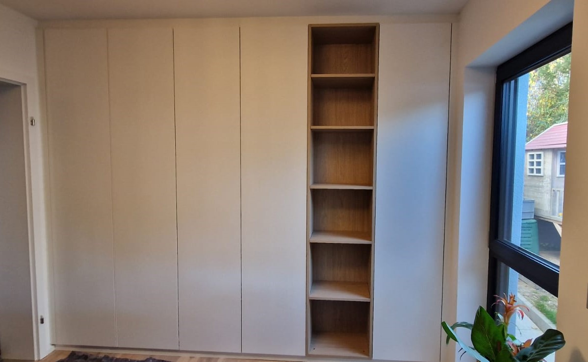Schlafzimmer-Einbauschrank in Wolkersdorf: Der weiße Schlafzimmer-Schrank wurde nach Maß gefertigt und in die Wand eingepasst. Ein offenes Regal in Eiche unterbricht die ansonsten gleichförmige Front.