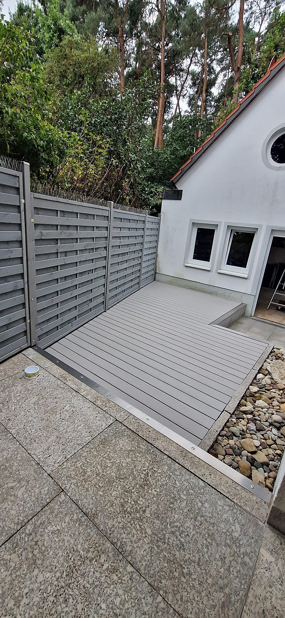 Nach der Terrassensanierung bei Erlangen: Terrasse aus grauen WPC-Dielen und Sichtschutz mit Taubenschutz aus grau lackiertem Holz.